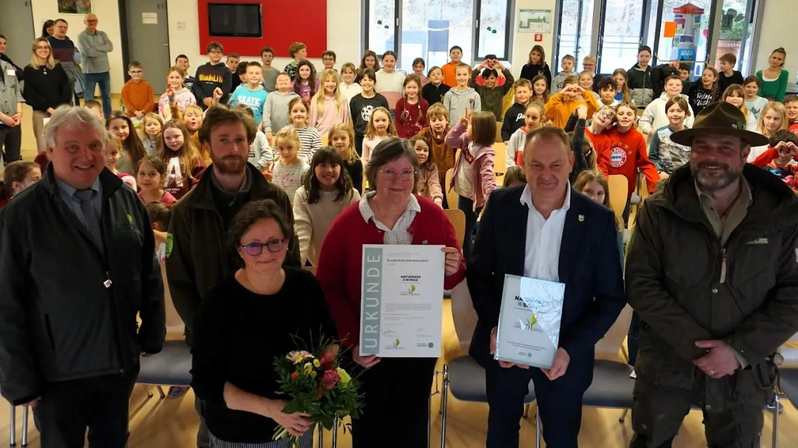Bild v.l.n.r.<br>Nach der Ehrung lauter strahlende Gesichter: Markus Dollacker (1. Vorsitzender Naturpark Hirschwald e.V.) , Ranger Jonas Nelhiebel, Isabel Lautenschlager (Geschäftsführerin), Bürgermeister Erich Meidinger, Ranger Christian Rudolf mit Begleithund „Ranger“, vorne Schulleiterin Ulrike Erlbacher. Im Hintergrund die begeisterten und naturverbundenen Schulkinder mit ihren Lehrkräften. <br> (Bild: Christine Wendl)