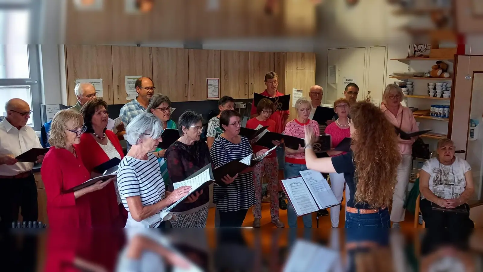 Mit seiner Serenade, die wegen des Wetters vom Garten ins Heim verlegt wurde, bereitete der Gemischte Chor unter Leitung von Jana Müller (am Dirigentenpult) den Bewohnern des BRK Seniorenwohn- und Pflegeheims St. Barbara und den Gästen einen stimmungsvollen und kurzweiligen Abend. Sitzend die Vorsitzende Renée Ehringer-Hoffmann. (Bild: Rudolf Wild)