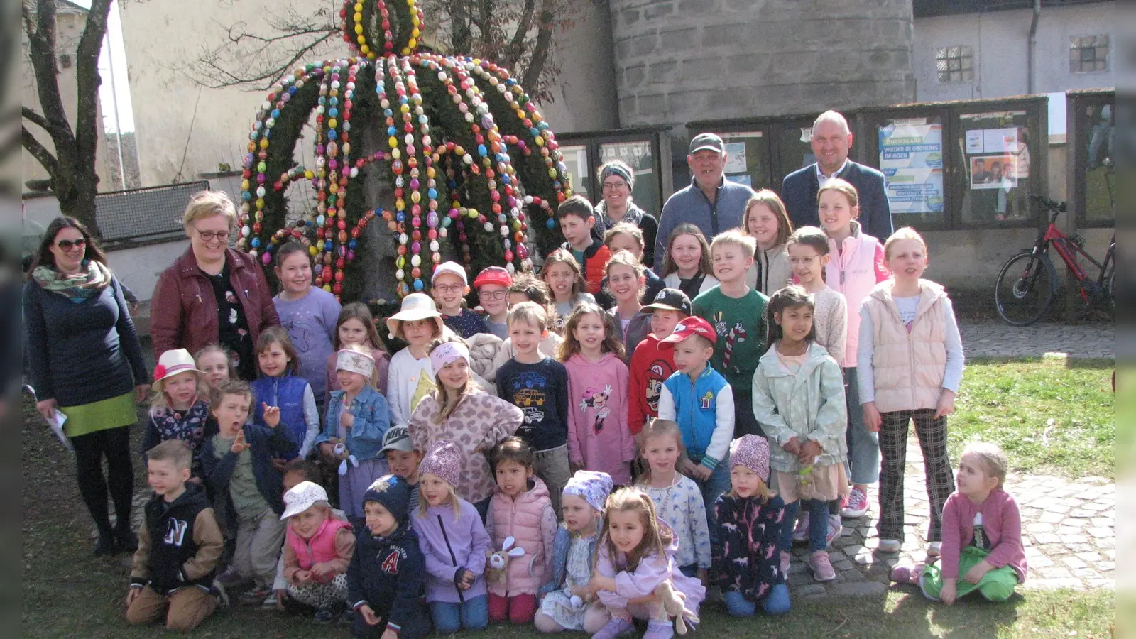 Bürgermeister Richard Kammerer (hinten rechts) dankte Georg Seiser (links daneben) von der Kolpingsfamilie für das Aufstellen des Osterbrunnens. Mit Liedbeiträgen zum Osterfest erfreuten die Kinder mit Leiterin Susanne Hausmann (2. v. l.) alle Anwesenden.  (Bild: Johann Kneißl )